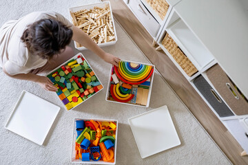 Young woman cleaning childish toy sorting wooden Montessori and plastic details box basket top view