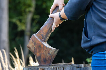 Close-up of a woman holding a wooden ax in her hand on a tree stump in autumn