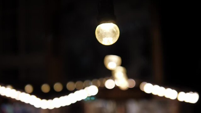 Hanging rows of garlands with light bulbs and a carousel rotating in the dark. Glowing light bulbs at night in the destruction park.