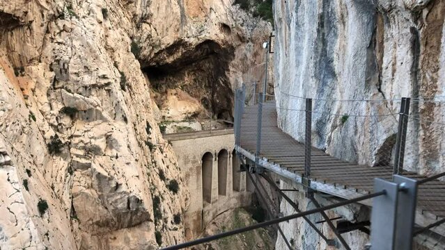 Reveal shot of a train passing through a rocky cliff tunnel in Caminito del Rey, El Chorro, Spain.