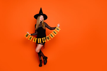 Full length photo of funky carefree lady wear black wizard costume cap hanging halloween flags...