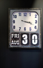 Rectangle, wooden, retro analogue clock with day, date and month functions on dark wall.