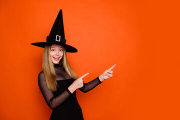 Photo portrait of pretty blonde teenager girl point empty space dressed black halloween outfit isolated on orange color background