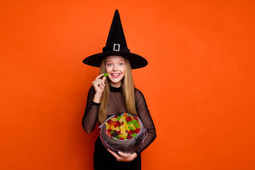 Photo of excited funky girl dressed dark witch dress headwear eating marmalades empty space...