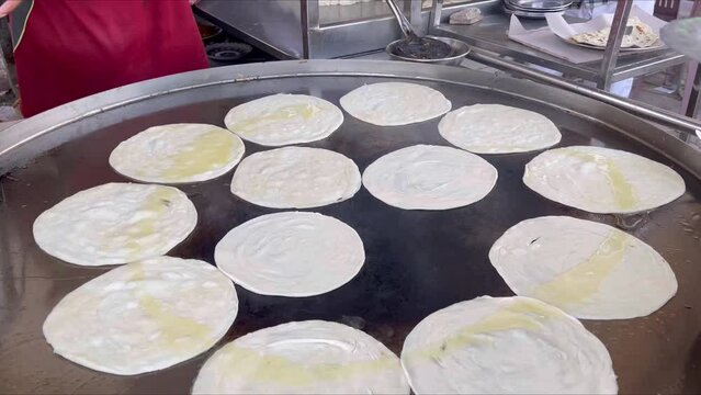 Expert bread maker making parathas and oiling them on a big frying pan - Pakistan street food