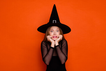 Photo of excited scared girl dressed dark witch dress headwear celebrating halloween isolated orange color background