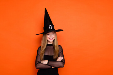 Photo of positive pretty girl dressed dark witch dress headwear smiling arms crossed empty space isolated orange color background