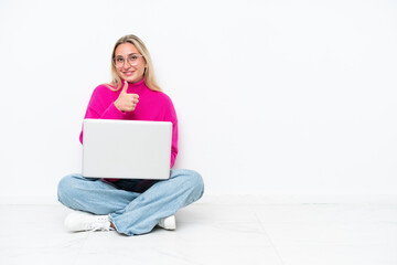 Young caucasian woman with laptop sitting on the floor giving a thumbs up gesture