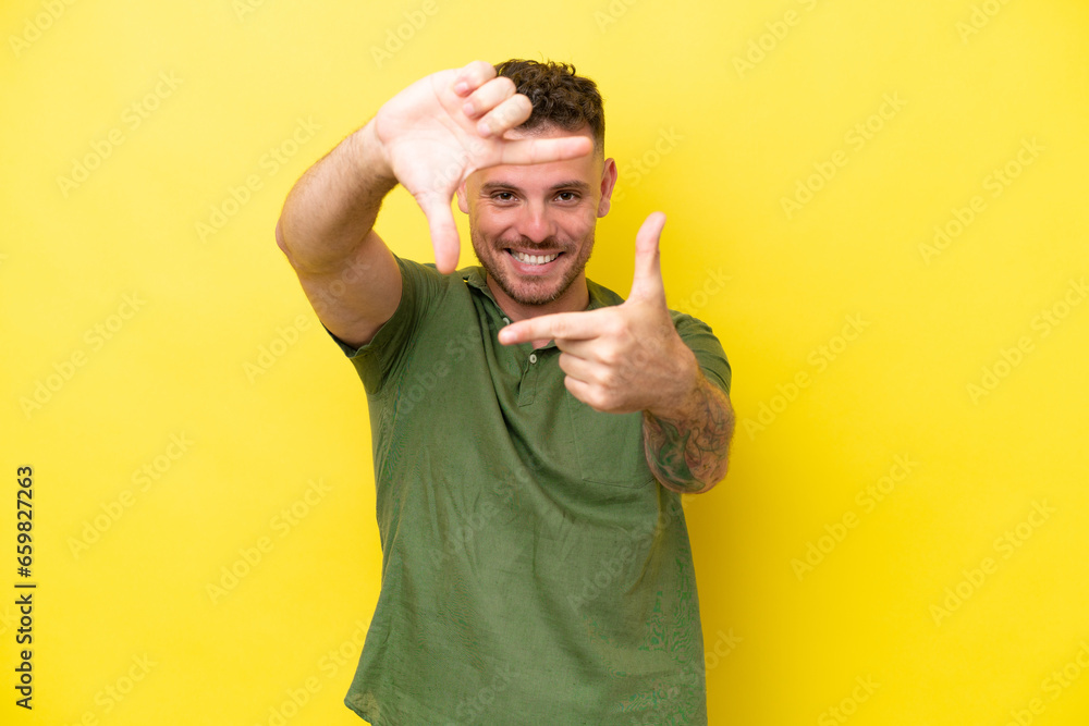 Wall mural young caucasian handsome man isolated on yellow background focusing face. framing symbol