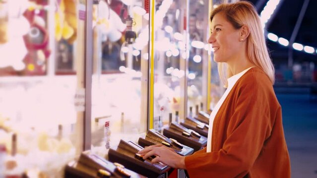 Girl plaing claw machine on a fun fair amusiment park. Night fair illumination, Ferris wheel spinning in the background. Fun for the whole family