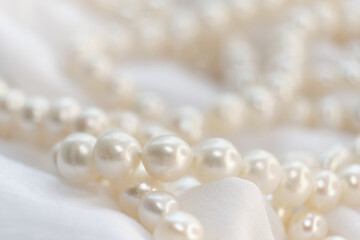 A cascade of pearls rests on a soft, white cloth, their natural luster dimly reflecting light. The...