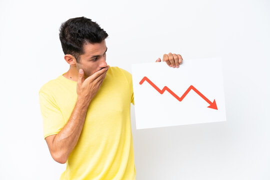 Young handsome man over isolated white background holding a sign with a decreasing statistics arrow symbol with surprised expression
