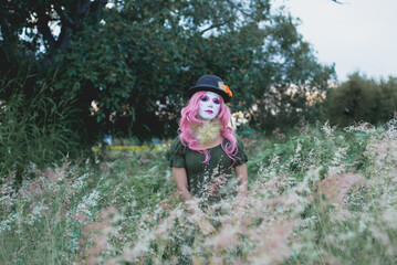 Young woman made up as a sad clown in a lonely field. Concept of loneliness and sadness. Halloween...