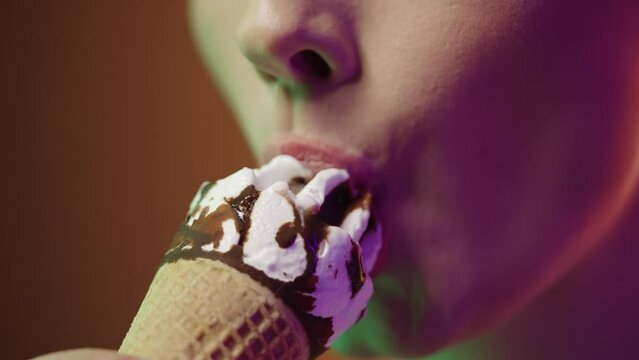 Close up of a young woman eating a vegan cream ice cream with vegan chocolate and enjoying the delicious taste in front of black and yellow background in slow motion