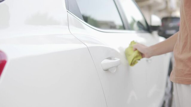 A woman wipes dirt from a white car with a rag.