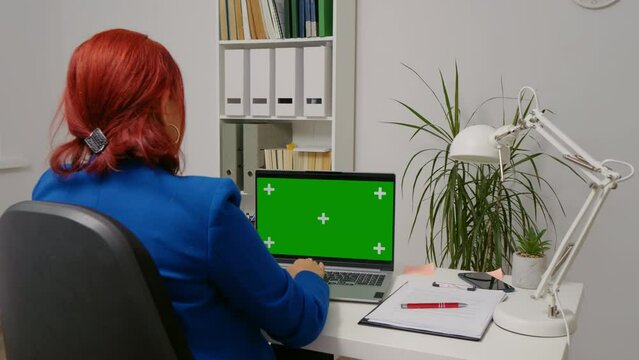Business woman sitting working on laptop with mock up green screen chroma key display. Office person using laptop with green screen, sitting at table