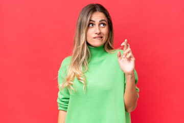 Young Uruguayan woman isolated on red background with fingers crossing and wishing the best