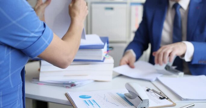 Business man and woman sitting at table and sorting documents with stapler and hole punch 4k movie. Paper work concept