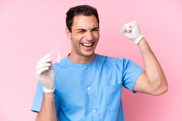 Dentist caucasian man holding invisible braces isolated on pink background celebrating a victory - obrazy, fototapety, plakaty