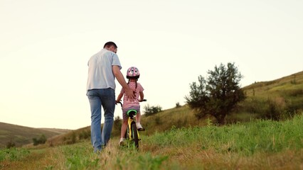 Supportive father takes care of preschooler girl learning to ride bicycle in field