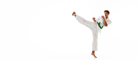Young man, karate, taekwondo athlete in kimono and green belt training isolated on white studio...