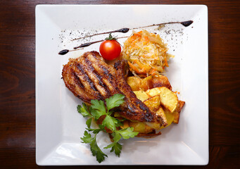 Top view on Grilled bone-in steak served with fried potatoes, stewed cabbage and cherry tomatoes on a white square plate