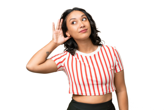 Young Argentinian woman over isolated background listening to something by putting hand on the ear