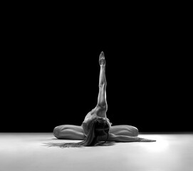 Beautiful nude sexy fitness girl with a great muscular figure flexing her perfect body in a yoga pose at the strange studio. Black and white photo.
