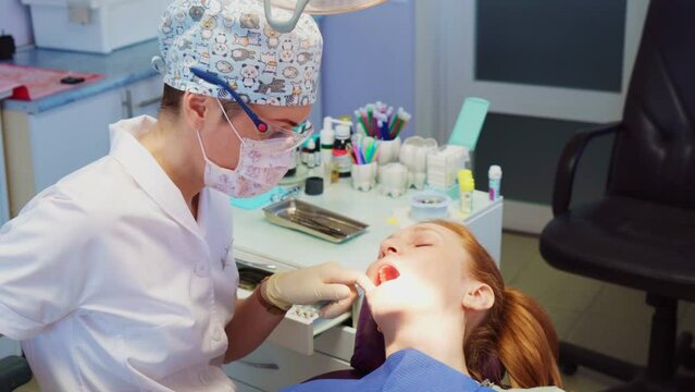 A female dentist treats the teeth of a red-haired girl in a dental clinic. Oral health and hygiene concept.