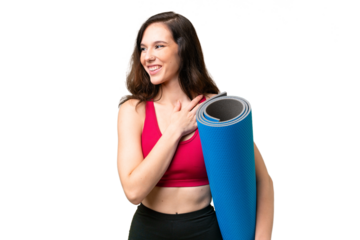 Young sport woman going to yoga classes while holding a mat over isolated background looking up while smiling