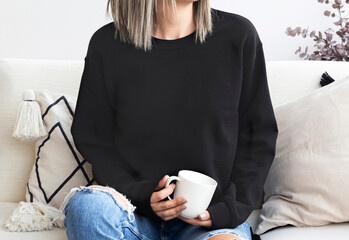 Girl in template blank black sweatshirt home,  coffee design. Black hoodie 18000 model mock up blank, empty, copy space

