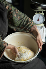 Woman kneading homemade yeast dough in bowl holding it on her knees.