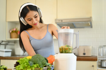 Obraz na płótnie Canvas Charming young woman in headphone making healthy smoothie in kitchen. Healthy lifestyle concept