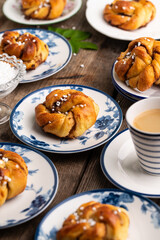 Homemade traditional Swedish cinnamon buns (swirls) on separate white and blue porcelain plates and cup of espresso coffee on wooden table.