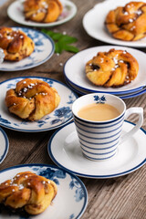 Homemade traditional Swedish cinnamon buns (swirls) on separate white and blue porcelain plates and cup of espresso coffee on wooden table.