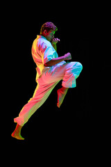 Professional martial arts athlete in motion, training, practicing karate over black studio background in neon lights. Concept of martial arts, combat sport, energy, strength, health. Ad