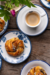 Homemade traditional Swedish cinnamon buns (swirls) on separate white and blue porcelain plates and cup of espresso coffee on wooden table.