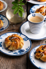 Homemade traditional Swedish cinnamon buns (swirls) on separate white and blue porcelain plates and cup of espresso coffee on wooden table.