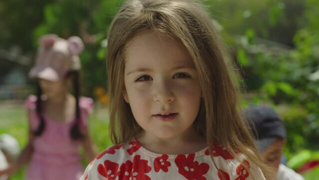 Portrait of beautiful and adorable kid . Girl face in park close up. Portrait Little Child Girl Looking at Camera Standing in garden with children . Dream girl . Child smiles at camera . Slow Motion