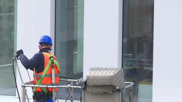 Worker wearing safety harness wash office building facade at height