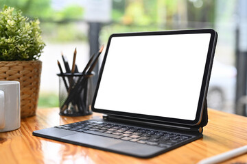 Digital tablet with blank screen, pencil holder, coffee cup and houseplant on wooden table