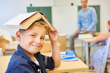 Funny boy with a book on his head in a classroom as class clown