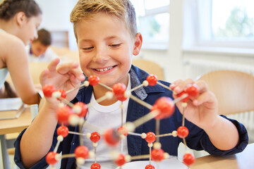 Smiling schoolkid touching molecular structure in class