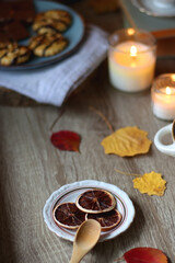 Fototapeta na wymiar Cup of tea or coffee, plate with desserts, dried oranges, bowl of grapes, scented candles, vintage books, pumpkins and autumn leaves on the table. Autumnal hygge. Selective focus.