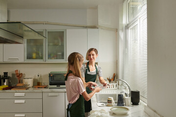 Teenage girl helping mother to wash dishes after cooking