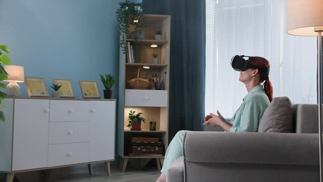 modern technology, a young woman uses Viar glasses and communicates with power of a call and virtual reality with friends while sitting on sofa at home