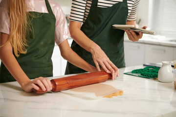 Obraz premium Cropped image of mother explaining teenage daughter how to roll out cookie dough