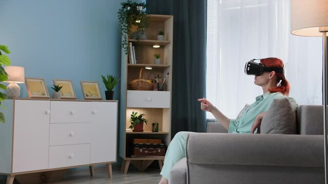virtual reality, young woman in vair glasses uses modern technology and browses Internet while sitting on sofa in the room