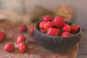 A close-up view of strawberries in a coconut bowl lying on a wooden board.