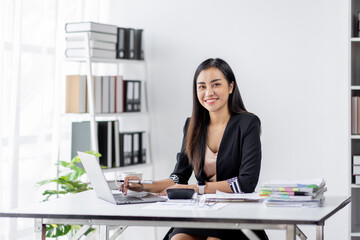 Asian Businesswoman Using laptop computer and working at office with calculator document on desk, doing planning analyzing the financial report, business plan investment, finance analysis concept.
